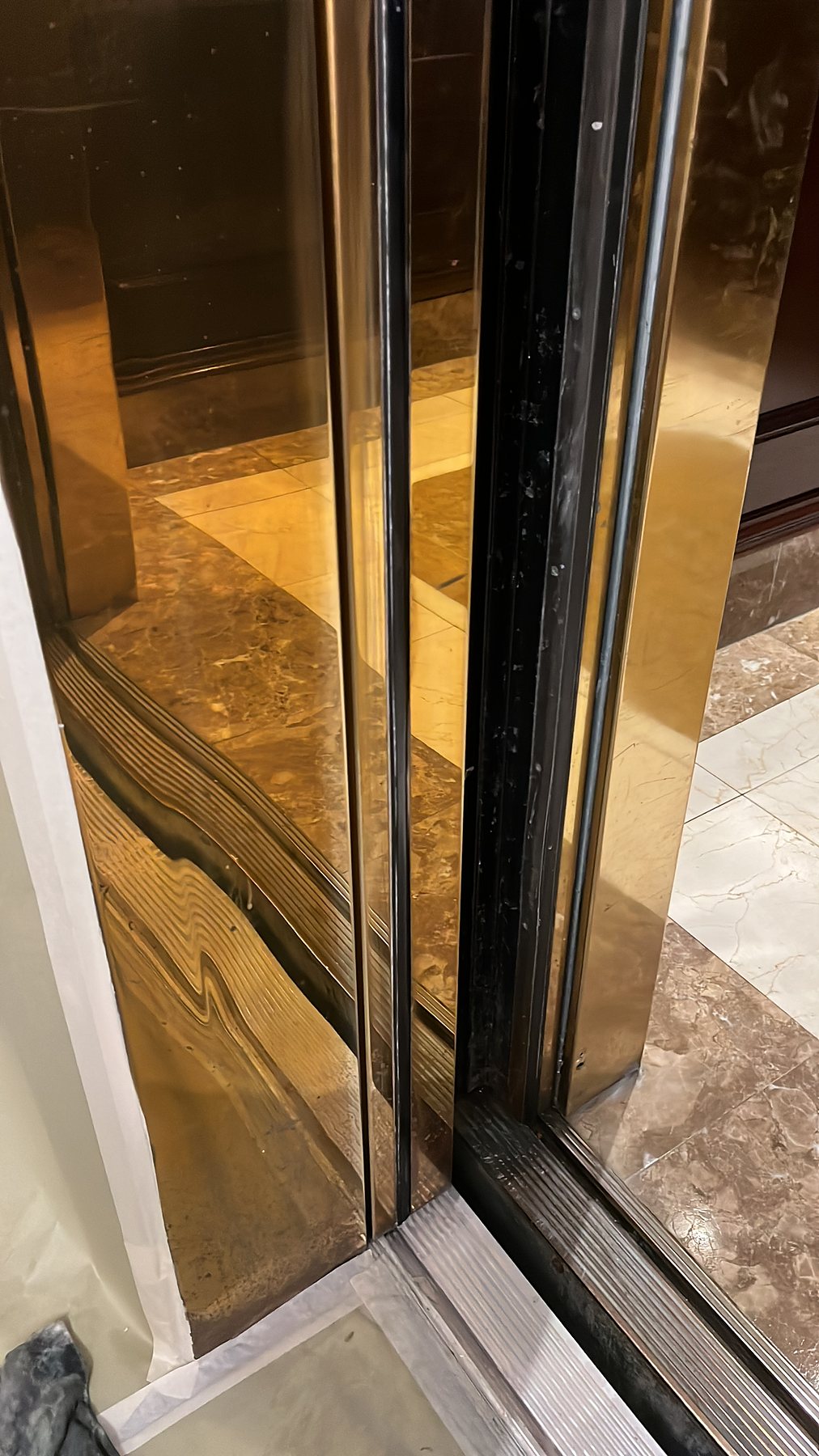 Mirror-polished brass elevator door frame reflecting a marble lobby floor